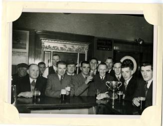 Black and white photograph Of Group At Bar With A Trophy. Possibly A Hall Russell Football/Bowl…