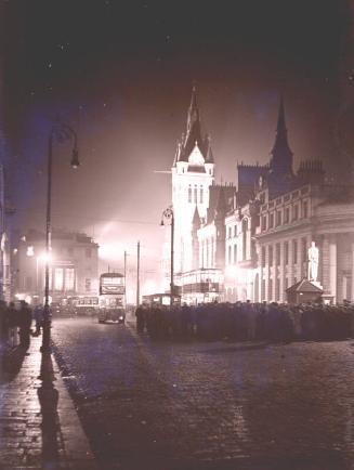 Photograph of the Town House as night with crowd and Tram car.