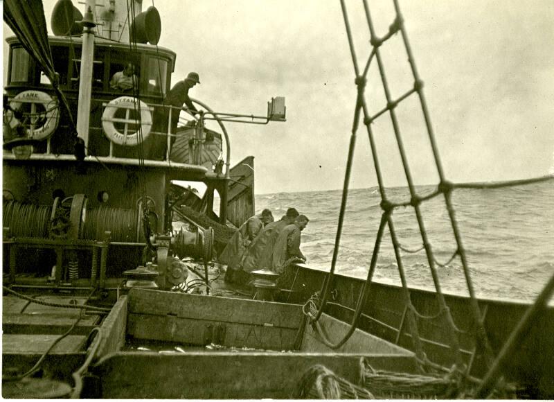 Black and white photograph showing men, in oilskins, hauling nets