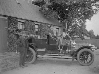 Motor car with driver at wheel and another man standing by