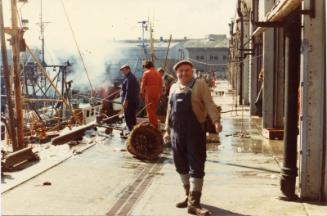 Colour Photograph Showing Aberdeen Fish Market, With Vessels Docked. A Man In Dungarees Poses