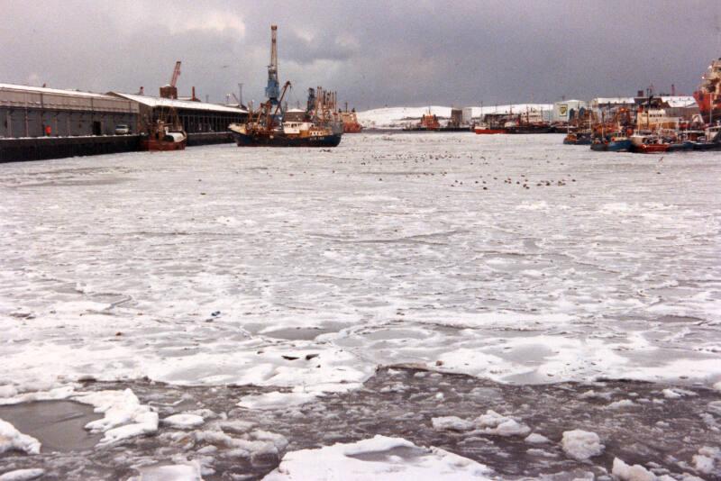 Colour Photograph Showing The Harbour Frozen Over With Ice, Some Fishing Vessels