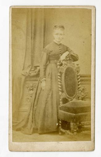 Standing young woman leaning on chair