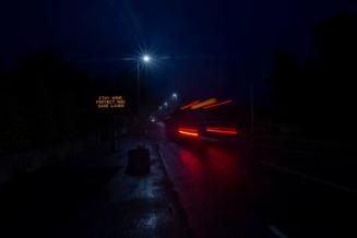 Digital photograph of an illuminated 'stay home and protect lives' sign next to a bus.