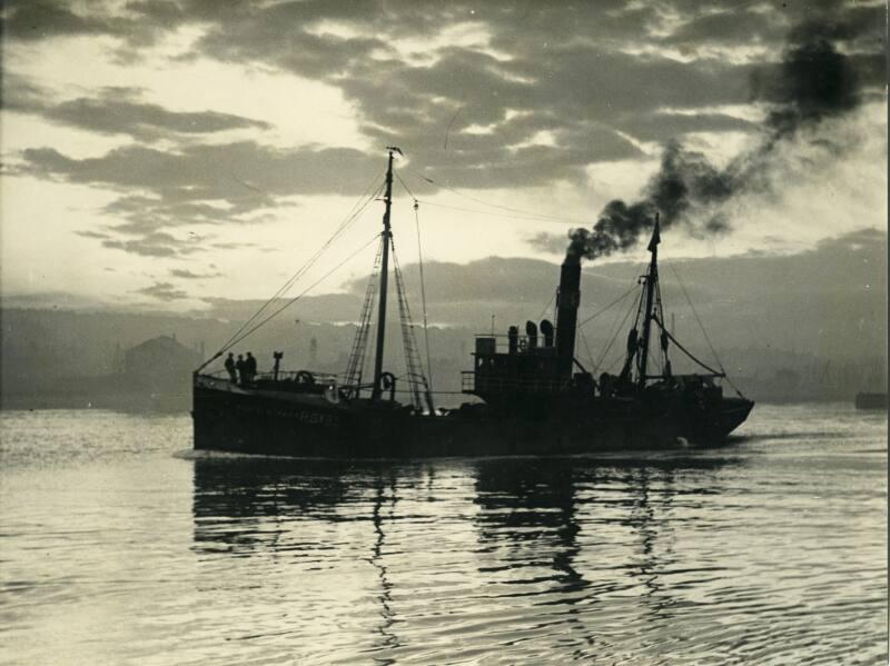 Black and white photograph showing Aberdeen Harbour in the 1930s, trawler leaving harbour in the evening