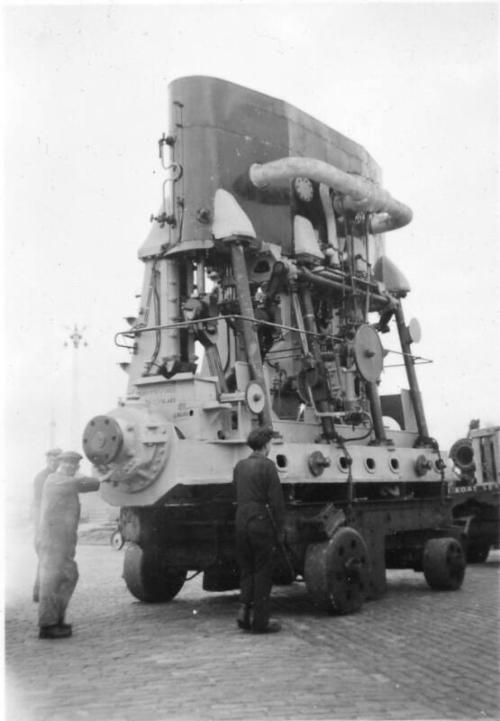 Black and White Photograph in album of ship's engine on flat-bed loader being exported to Poland