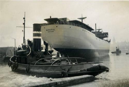 Black and White Photograph in album of cargo ship 'Nordpol' stern view with tug 'Danny'