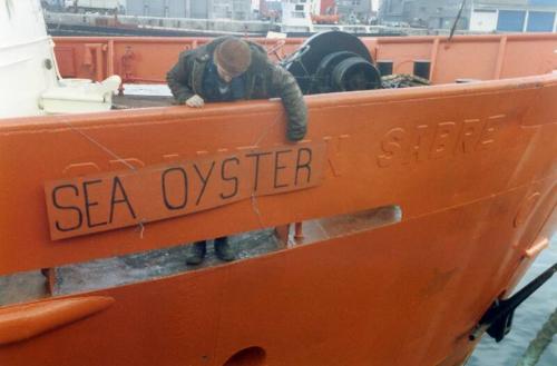 Colour Photograph Showing Man Adjusting A Temporary Namesign 'sea Oyster'over Painted Out Name On Ship